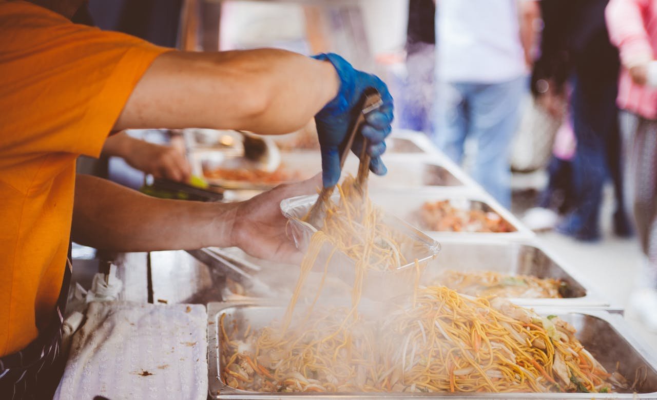 A street vendor serving freshly cooked noodles at a bustling outdoor market.